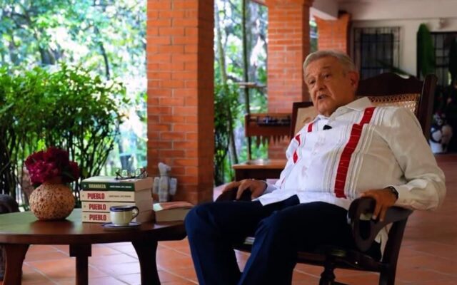Andrés Manuel López Obrador sentado junto a varios ejemplares de su libro Pueblo
