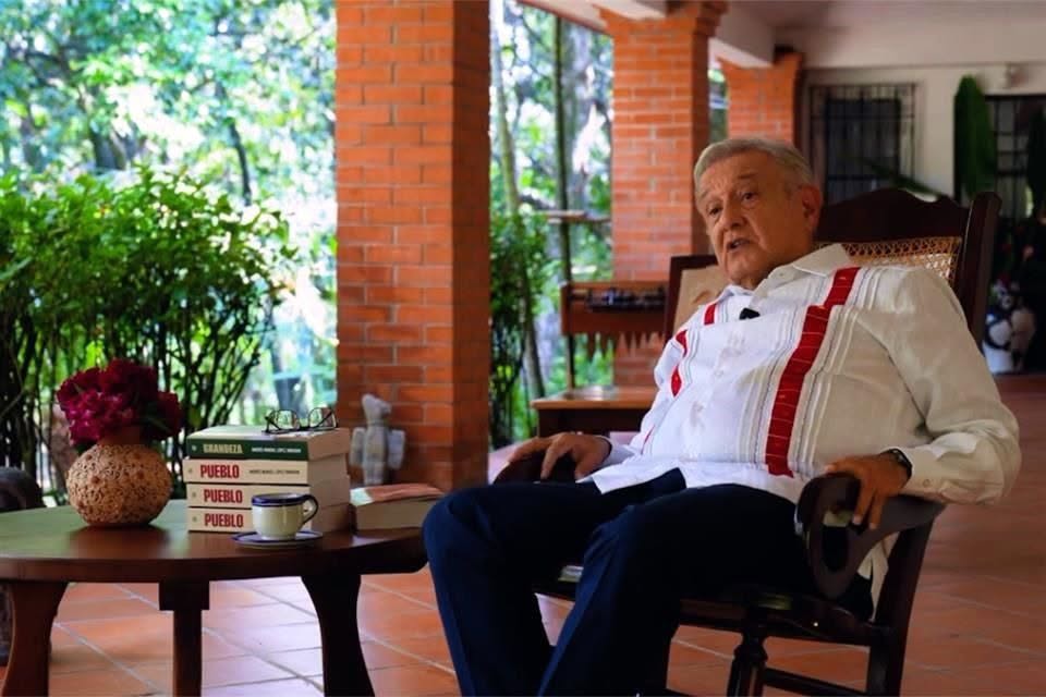 Andrés Manuel López Obrador sentado junto a varios ejemplares de su libro Pueblo